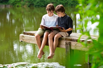 Zwei jungendliche Freunde lesen ein Buch am Teich Sommerferien